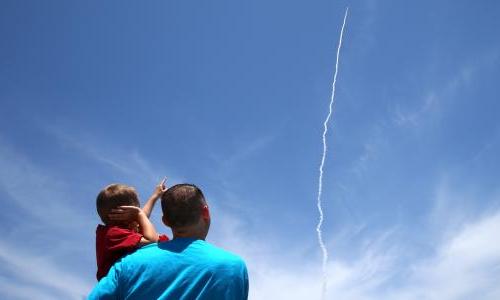 一个被父亲抱着的小男孩指着天空中导弹的烟雾痕迹.
